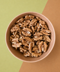 A top-down view of shelled walnuts piled in a small round brown bowl, set against a split green and brown background.