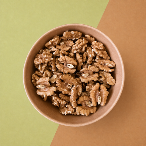 A top-down view of shelled walnuts piled in a small round brown bowl, set against a split green and brown background.